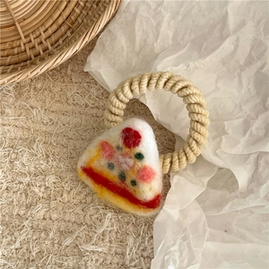 Detail of wool felt pizza hair tie on beige fabric with rustic straw basket background