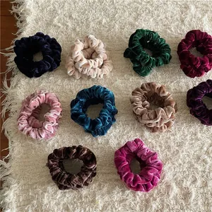 Set of 10 colorful velvet scrunchies in various shades on a soft white carpet background