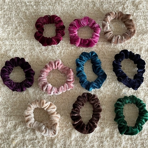 Flat lay of ten colorful velvet scrunchies in varied shades on a soft beige background