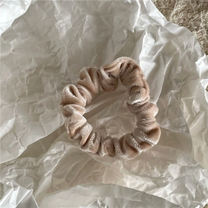 Detail view of apricot velvet scrunchie showing soft texture and pleated design on paper