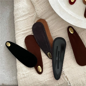 Detail of suede teardrop hair clips with gold handmade tags in earthy autumn colors