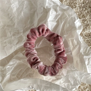 Detail of soft dusty pink velvet scrunchie placed on white crumpled paper