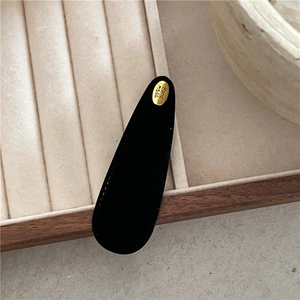 Close-up of black suede teardrop clip with a golden Handmade metal logo on velvet
