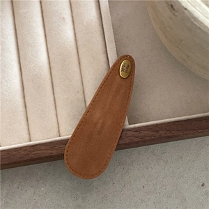 Macro detail of a brown suede teardrop hair clip with a gold handmade metal tag