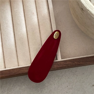 Close-up of red suede hair clip with a gold metallic 'Hand made' engraved tag