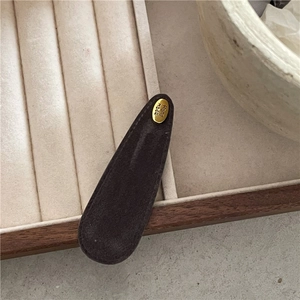 Close-up of a dark brown suede BB hair clip with a golden engraved Hand Made metal plate