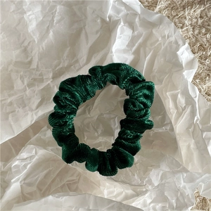Detailed view of a dark green velvet scrunchie with soft texture on white paper