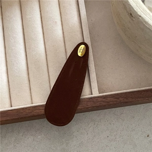 Detailed view of handmade gold label on brown suede water-drop hair clip in jewelry tray