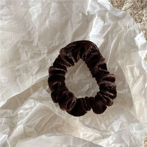 Close-up of a soft dark brown velvet scrunchie showing fine texture and shiny fabric