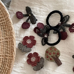 Detailed view of handmade knitted cherry and flower hair clips on white linen fabric