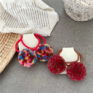 Detail von bunten Plüsch-Pom-Pom-Haargummis in Rot und Braun auf einer Displaykarte