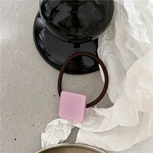 Gros plan d'un chouchou minimaliste carré en acétate rose avec élastique marron