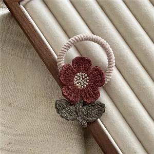Detail of handmade crochet flower hair tie with reddish-brown petals and green leaves