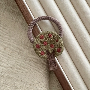 Close-up of embroidered green tree design with red fruit on a plush purple hair scrunchie