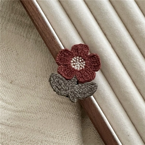 Detailed view of handcrafted crochet flower and green leaves on soft white velvet surface