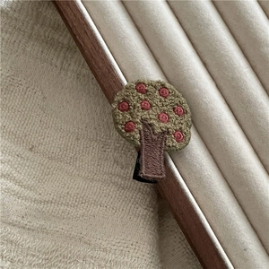Detailed embroidery of a green tree hair clip with red fruits and metal duckbill clip