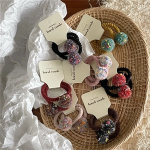 Detail of colorful plush ball hair ties with handmade card in a rustic woven tray