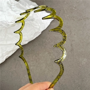Macro shot of green wavy hairband featuring black marble texture and secure grip teeth