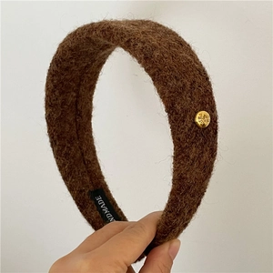 Gros plan sur un bandeau en laine marron avec boucle en métal doré et étiquette fait main
