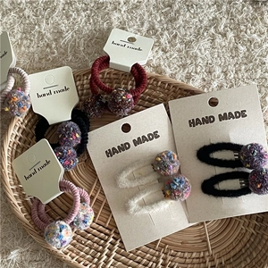 Detailed close-up of handmade hair ties and clips with colorful plush balls in a basket