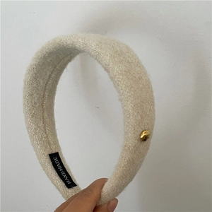 Détail du serre-tête en laine rembourré beige avec étiquette et bouton doré