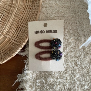 Close-up of handmade brown felt BB hair clips with colorful plush balls on a rustic mat