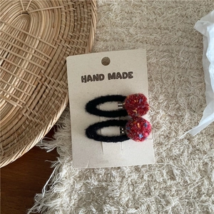Close-up of handmade red pom-pom hair clips set on card display with woven background