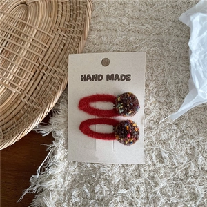 Close-up of handmade felt hair clips with colorful wool pom-poms on display card
