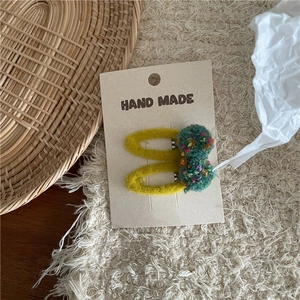 Detailed view of handmade yellow crochet hair clips with green pom poms on craft card