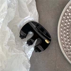Détail d'une pince à cheveux noire brillante avec étiquette dorée faite à la main sur le côté