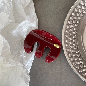 Détail d'une pince à cheveux bordeaux brillante avec une étiquette dorée Hand Made ronde