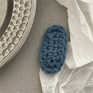 Macro detail of hand-knitted blue oval hair clip showing intricate yarn weave texture