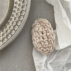 Detail of cream oval knitted hair clip made of thick cotton yarn on a modern stone tray