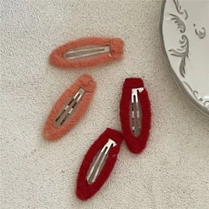 Detailed view of red and orange plush fabric BB hair clips set on a textured white background