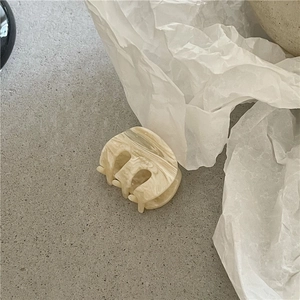 Close-up of a small oval hair claw clip with beige marble texture and acetate material