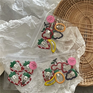 Detail of fruit oil-drop hair clips in gift packaging with strawberry and cherry patterns