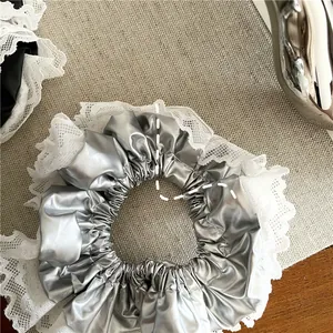 Détail de chouchou en PU argenté avec bordure en dentelle blanche sur fond tissé beige