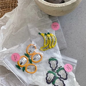 Retail packaging of fruit hair clips with banana and grape designs and a thank you sticker