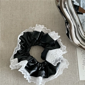 Gros plan sur un chouchou en cuir PU noir avec bordure en dentelle blanche et fini brillant
