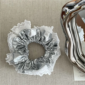 Gros plan d'un chouchou argenté métallisé avec bordure en dentelle sur tissu texturé gris