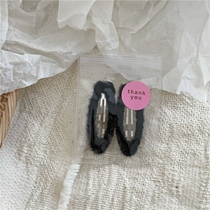 Detail of two black plush faux fur BB hair clips in clear gift packaging with sticker