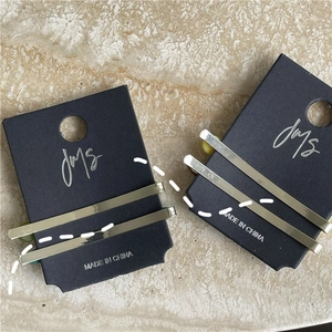 Close-up of minimalist gold metal hair clips on black display card over marble background