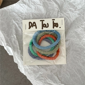 Détail de cinq chouchous plissés colorés aux tons pastels avec leur emballage carton