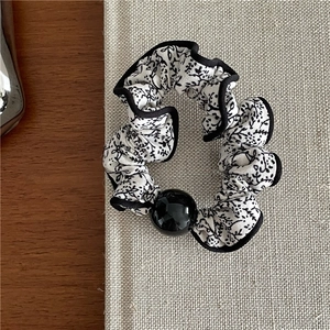Detailed shot of black and white floral scrunchie with a glossy black decorative bead