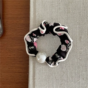 Detail of floral fabric scrunchie with pink blossoms, wavy white trim and a white pearl