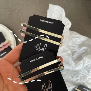 Close-up of dual minimalist gold hair clips on black cards with sleek polished metal finish