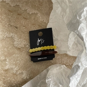 Close-up of yellow wavy acetate hair clip and brown barrette with text on a card