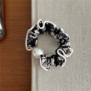 Detailed view of floral scrunchie with white pearl and wavy border on black fabric