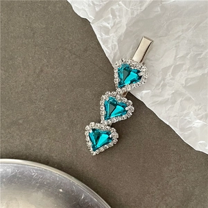 Macro detail of silver hair clip featuring three sparkling blue heart-shaped rhinestones
