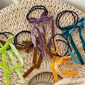 Set of five colorful velvet bow hair ties with long ribbons on a woven mat